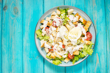 Fresh caesar salad in plate on blue wooden table. Top view