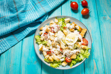 Fresh caesar salad in plate on blue wooden table.