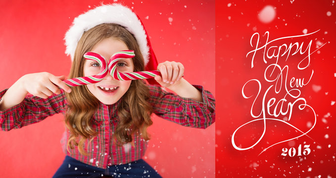 Happy little girl in santa hat holding candy canes against red vignette