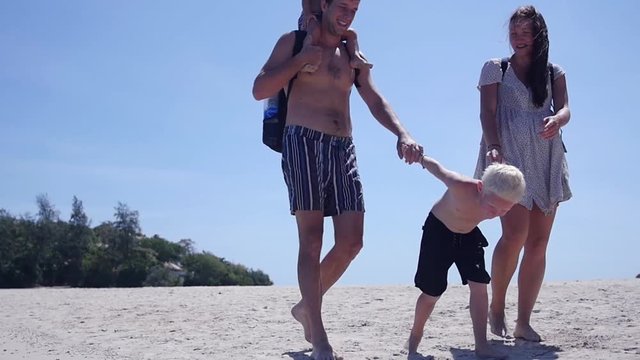 Mom and Dad hold his son by the arms and walk along the beach to the sea, the daughter sits on his father's shoulders. slow motion, 1920x1080, full hd