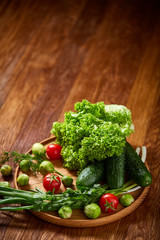 Vegetarian still life of fresh vegetables on wooden plate over rustic background, close-up, flat lay.