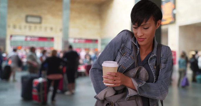 Gorgeous African woman takes her smartphone out of her purse to see a recent text message, Young African-American female at train station lobby with coffee checks her phone, 4k