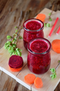 Red vegetable smoothie made of carrot and beetroot in glass jars on wooden background