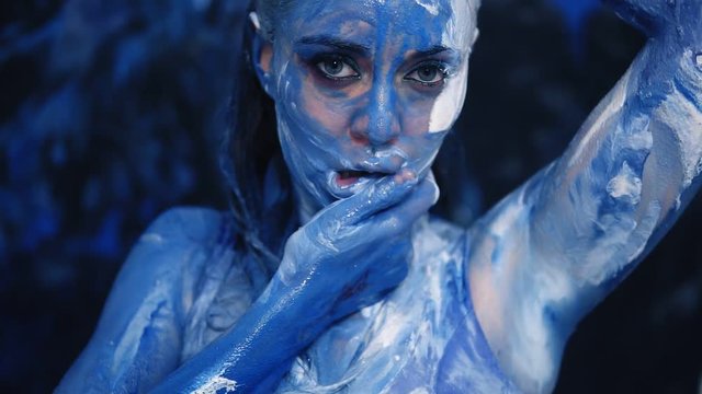 Close up footage of a beautiful, seductive woman's body. Smearing blue and white paint up down her body. Sexy