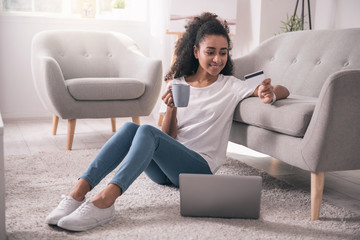 At home. Pleasant joyful woman sitting on the floor while doing shopping at home