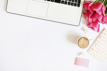 Feminine office desktop with black & white laptop keyboard, pink tulip flowers bouquet, cup of coffee w/ latte art, pen, notebook computer, various supplies. Background flat lay, copy space, close up.