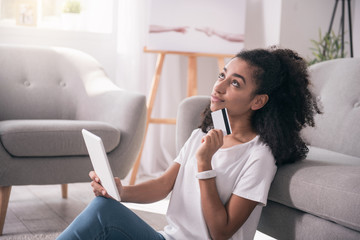 Internet banking. Nice dreamy woman looking up while thinking about what to buy online