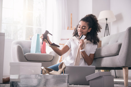 I need more. Delighted positive woman buying a new pair of shoes while being shopping addicted