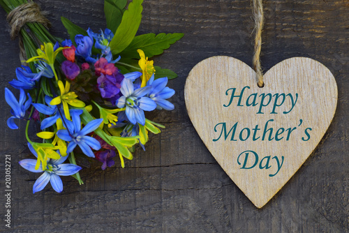 Happy Mother's Day greeting card with spring flowers bouquet and decorative heart on old wooden background. Selective focus.
