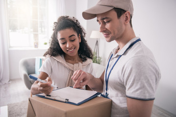 Obraz premium Sign here. Joyful delivery man pointing with his finger at the document while showing where to sign the document