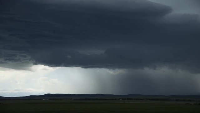 Downpour out of gray clouds onto low rolling hills, time lapse