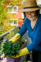 Eine Frau mittleren Alters pflanzt Kräuter und Blumen auf dem Balkon