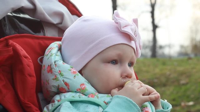 A thoughtful little girl is sitting in a stroller and touching the nipple with her hands