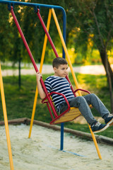 A little boy in a striped T-shirt is playing on the playground, Swing on a swing.