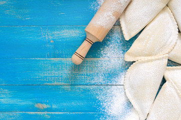 Not fried chebureks in flour on a blue wooden table. Traditional Turkic-Mongolian dish. Frozen semi-finished products. Free space for an inscription.