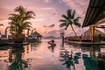 young man at the beach during vacation at the tropical islands of the Seychelles, men in infinity pool during sunset at the Seychelles La Digue Island - obrazy, fototapety, plakaty