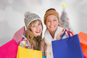 Beautiful women holding shopping bags looking at camera  against blurry christmas tree in room