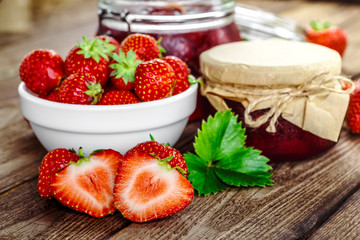 Homemade strawberry jam or marmalade in the glass jar and the basket of ripe strawberries on the wooden table