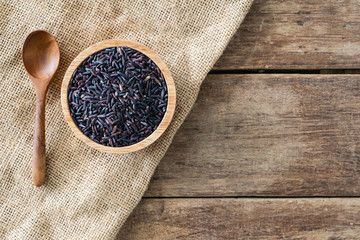 raw deep purple organic riceberry in wood bowl with wood spoon on gunny sack cloth on wooden table,...