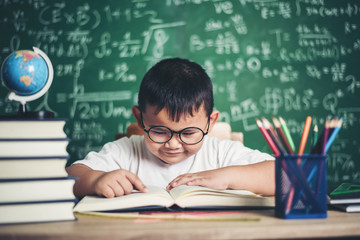 boy reading a book sitting at the table in the classroom