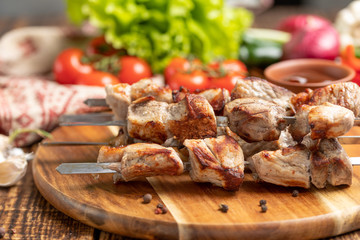 Juicy kebabs from pork on skewers laid out on a decorative board with fresh vegetables.