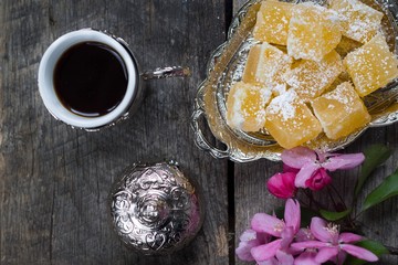 tasty orange lokum, turkish coffee and pink flowers on wooden background