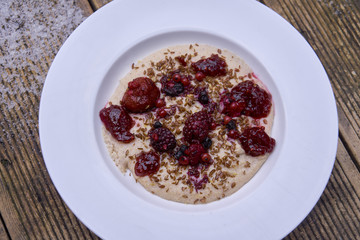 Vegan semolina porridge presented on wooden table with snow in the background. The porridge has berries and seeds on top.