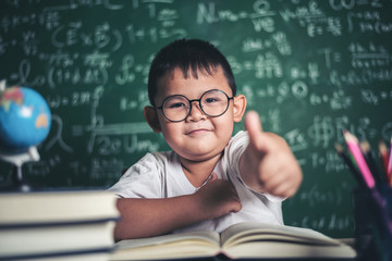 Portrait of a boy with hands thumbs up in the classroom.