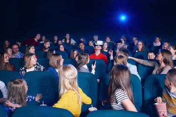 View of audience watching film in movie theatre. Boy in virtual glasses sitting in centre. Curious ...