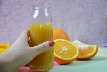 Woman hand with freshly squeezed orange juice in a bottle and orandes on colour background