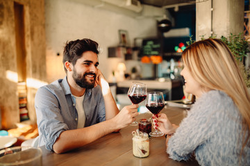 Cheers! Young handsome man is drinking wine with his girlfriend in cafe