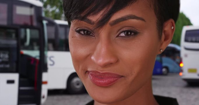Female African tourist stands outside at a tour bus stop in Paris, France, Pretty ethnic young lady on vacation in France looks at the camera with delight near some buses, 4k