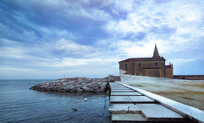 Santuario Madonna dell'Angelo  a Caorle con scogliera sul mare e cielo terso e nuvole