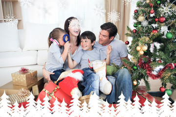 Happy family playing with Christmas gifts against fir tree forest and snowflakes