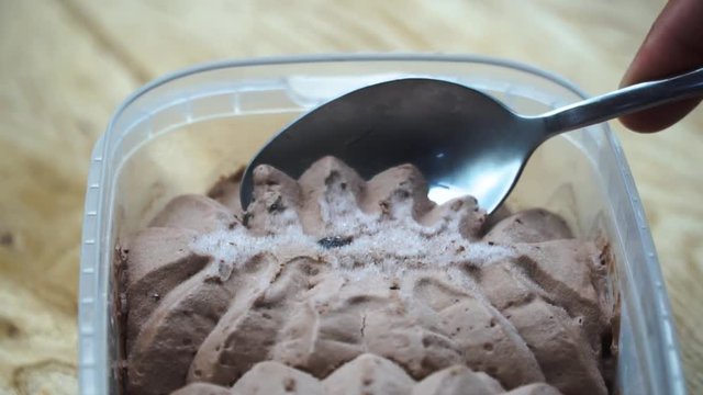 Ice cream scooped out of container with spoon. Wooden table. 