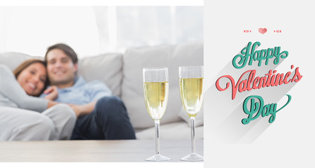 Couple resting on a couch with flutes of champagne against valentines day greeting