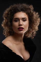 Fototapeta premium Sexy curly woman posing in the studio and looking at camera. Looking beatiful and passionate. Wearing light day make up and saturated violet lipstick on plump lips. Black background.