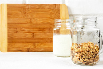 Grnola, raisins, milk in glass jars and various ingredients for a super meal with copy space on a light background