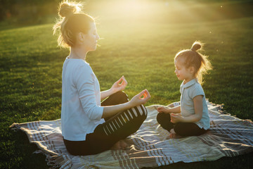 Mother practicing yoga with her daughter in the open air.