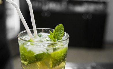 Closeup glass of unalcohol mohito cocktail with lime and mint and with a two tubes at bar background. Fresh drink for everybody. Freshy summer drink.