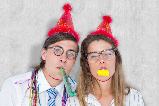 Geeky hipster wearing a party hat with blowing party horn against white background