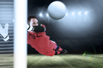 Fit goal keeper jumping up against football pitch under spotlights