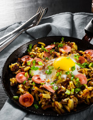 fried egg with sausage and potato in a frying pan on wooden table