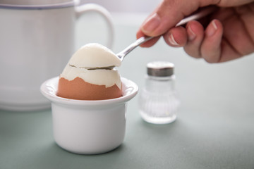 Frau löffelt gekochtes Hühnerei beim Frühstück im Eierbecher mit Eierlöffel