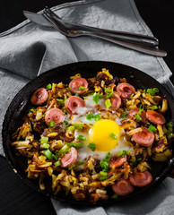 fried egg with sausage and potato in a frying pan on wooden table