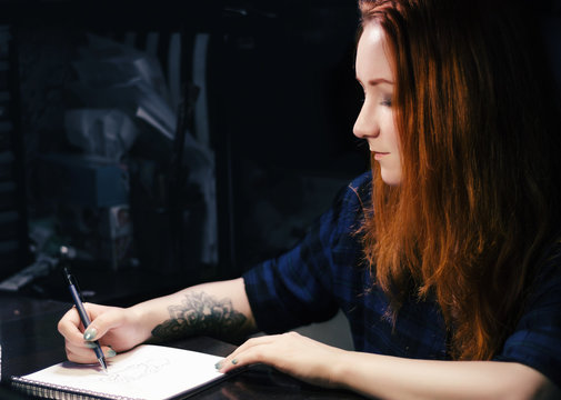 Artist designer jeweler girl draws a sketch of unusual jewelry ornaments with a pen on white paper. Home workshop