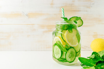 Detox water infused with sliced lemon, cucumber and sprigs of mint on wooden background.