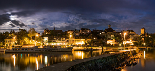 skyline at night  of Murten in Switzerland with the harbor and pier and boat in the foreground
