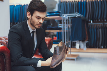 Young successful man in suit buys Oxford shoes sitting in fitting room.