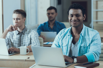 Happy students sitting at desks interact with laptop and tablet computer and reads books.